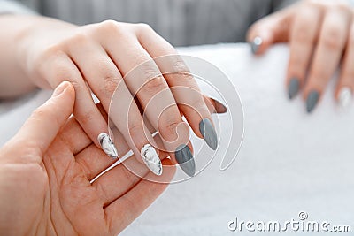 Beauty master manicurist do manicure to client. Closeup acrylic artificial nails painted in gray and marble design during manicure Stock Photo
