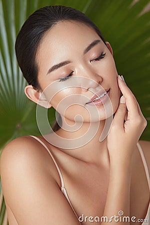 Beauty. Model Face On Palm Background. Asian Woman With Closed Eyes Enjoying Smooth, Hydrated And Glowing Skin. Stock Photo