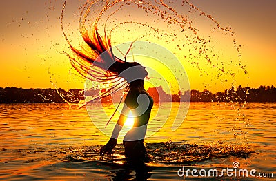 Beauty model girl splashing water with her hair. Girl silhouette over sunset sky. Swimming and splashing on summer beach Stock Photo