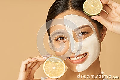 Beauty portrait of young woman with facial mask applied on half of her face holding slice of lime and lemon, posing Stock Photo