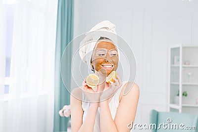 Beauty procedures skin care concept. Young woman with brown facial mud clay mask on her face in bathroom, with white Stock Photo