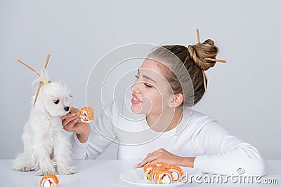 Beauty sexy woman with dog eating sushi. Sushi rolls. Fashion model girl eating Sushi with chopsticks. Perfect make up Stock Photo