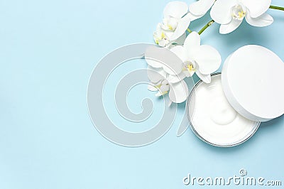 Beauty Spa concept. Opened plastic container with cream and White Phalaenopsis orchid flowers on blue background Flat Stock Photo