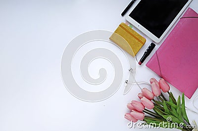 Beauty stuff. Makeup background. Aspects of makeup. Folder, tablet, tulips flowers, headphones, lipstick and closed notebook on th Stock Photo