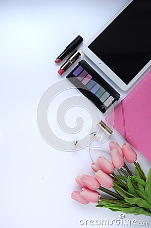 Beauty stuff. Makeup background. Aspects of makeup. Folder, tablet, tulips flowers, headphones, lipsticks and eye shadows on the t Stock Photo