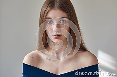 Beauty theme: portrait of a beautiful young girl with freckles on her face and wearing a blue dress on a white background in Stock Photo