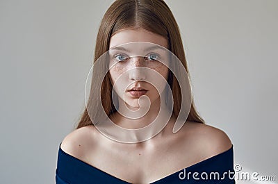 Beauty theme: portrait of a beautiful young girl with freckles on her face and wearing a blue dress on a white background in Stock Photo