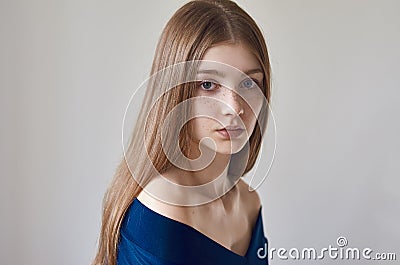 Beauty theme: portrait of a beautiful young girl with freckles on her face and wearing a blue dress on a white background in Stock Photo