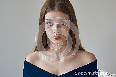 Beauty theme: portrait of a beautiful young girl with freckles on her face and wearing a blue dress on a white background in Stock Photo