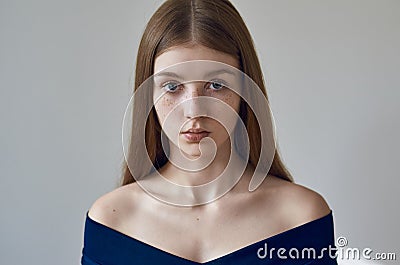 Beauty theme: portrait of a beautiful young girl with freckles on her face and wearing a blue dress on a white background in Stock Photo