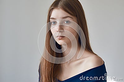 Beauty theme: portrait of a beautiful young girl with freckles on her face and wearing a blue dress on a white background in Stock Photo