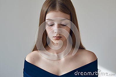 Beauty theme: portrait of a beautiful young girl with freckles on her face and wearing a blue dress on a white background in Stock Photo