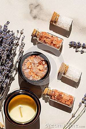 Beauty and wellness concept - sea salt in glass bottles and candle on wooden tray and bunch of lavender on marble background Stock Photo