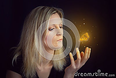 Beauty young blond hair woman hold hand under glowing orange butterfly. Photomanipulation glowing lepidopteran on black background Stock Photo