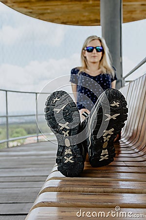 Beauty young caucasian blonde woman sit on bench, focus to shoes Stock Photo