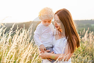 Beautyful woman with a little curly-haired boy in her arms stands in the middle of a field at sunset. Stock Photo