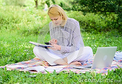 Become successful freelancer. Woman with laptop sit on rug grass meadow. Girl with notepad write note. Freelance career Stock Photo