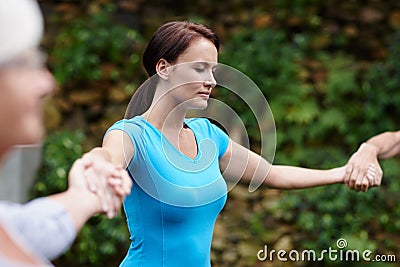 Becoming calm in the outdoors. a young woman holding hands with the people shes doing yoga with. Stock Photo