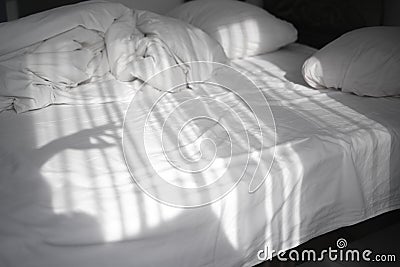 On a bed in a light bedroom the rays of the sun fall. reflection of curtains moving from the wind on crumpled bedding Stock Photo