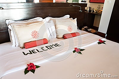 bed with white pillows and a coverlet, decorated with tropical flowers and an inscription - welcome. Theme of hotel service Stock Photo