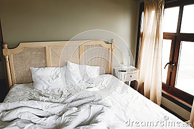 Bed with white sheets and vintage nightstand with decor at window in hotel room or provence home bedroom. Space for text. Stock Photo