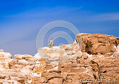Bedouin sitting on the peak of a high stone rock against a blue sky in Egypt Dahab South Sinai Editorial Stock Photo
