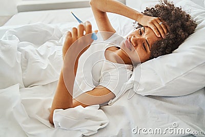 Bedridden woman holding a temperature-sensing device in her hand Stock Photo