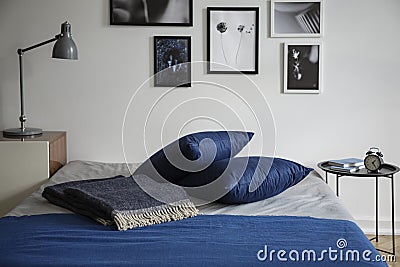 Bedroom interior with a warm wool blanket and navy blue pillows on a double bed by a white wall Stock Photo