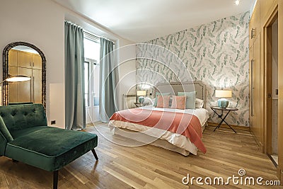 bedroom with king size bed with green velvet upholstered chaise longue seat, wooden floorboards in a vacation rental Stock Photo