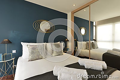 Bedroom with silver cushions, blue colored wall, fitted wardrobe with mirrored sliding doors and matching gold bedside tables with Stock Photo