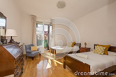 Bedroom with two single wooden beds, desk with drawers and closed folding top, blue armchair and balcony with views Stock Photo