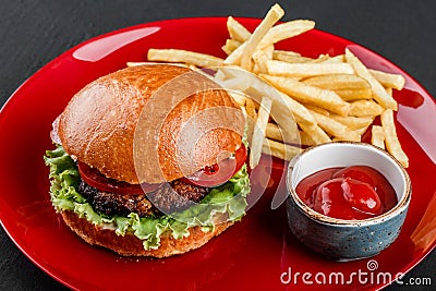 Beef burger and french fries with tomato sauce on red plate over dark background. Unhealthy food Stock Photo
