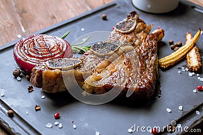 Beef ribs on bone on black stone with onion and little corn Stock Photo