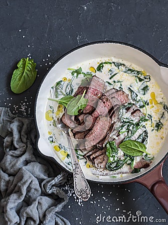 Beef steak and a creamy spinach sauce in a cast iron skillet on a dark background Stock Photo