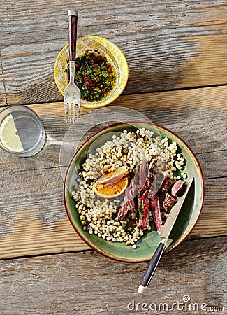 Beef steak grilled pearl barley couscous wooden table sauce water lemon top view Healthy dinner table concept Stock Photo