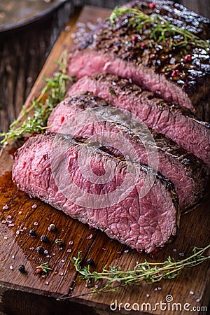 Beef steak. Juicy medium Rib Eye steak slices on wooden board with fork and knife herbs spices and salt Stock Photo