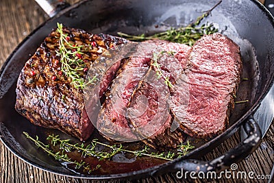 Beef steak. Juicy medium Rib Eye steak slices in pan on wooden board with fork and knife herbs spices and salt Stock Photo