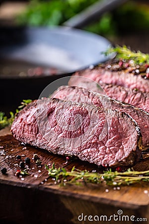 Beef steak. Juicy medium Rib Eye steak slices on wooden board with fork and knife herbs spices and salt Stock Photo