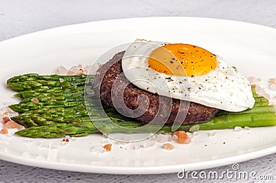 Beefsteak from minced beef with fried eggs and fresh green asparagus Stock Photo