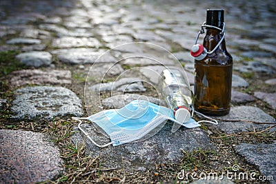 Beer and liquor bottles and a surgical face mask left on a cobblestone road, while bars have closed due to infection with Stock Photo