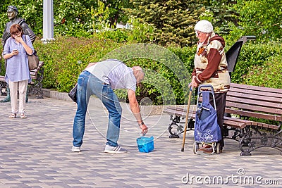 A beggarly elderly woman asks for alms on the embankment near a sculpture to Red Army soldier Sukhov Editorial Stock Photo