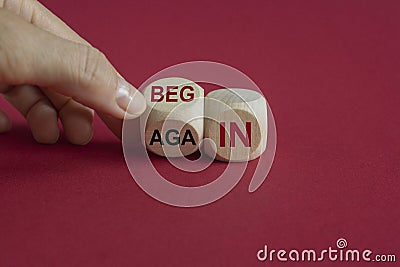 Begin again symbol. Businessman turns wooden cube and changes the red words begin to again. Beautiful red background. Business and Stock Photo