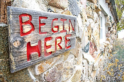 Begin Here Sign on a Rustic Building Stock Photo