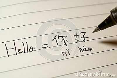 Beginner Chinese language learner writing Hello word Nihao in Chinese characters and pinyin on a notebook Stock Photo