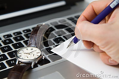 The beginning of the day, the clock on the laptop keyboard, hand holding a blue pen, workplace. Stock Photo