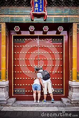 A couple peeking through the small opening in a door at the Forbidden City in Beijing China Editorial Stock Photo