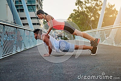Behind every strong man is a strong woman. a young woman balancing on her boyfriends back while doing pushups outdoors Stock Photo