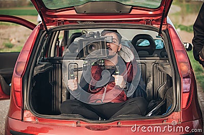 Behind scene improvisation. Cameraman from trunk of car shooting Stock Photo