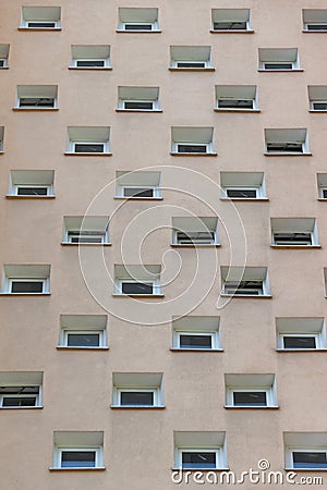 A beige building facade with small, uniformly arranged square windows in a grid pattern. Details and elements of architecture Stock Photo