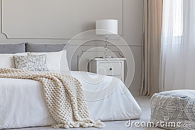 Beige woolen blanket on white duvet on king size bed in elegant bedroom interior Stock Photo